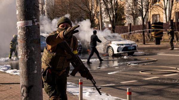 Ukrainische Soldaten beziehen Stellung vor einer Militäreinrichtung in der Hauptstadt, während Feuerwehrleute zwei brennende Autos löschen. Vor allem in Kiew droht eine Ausweitung der Kampfhandlungen.