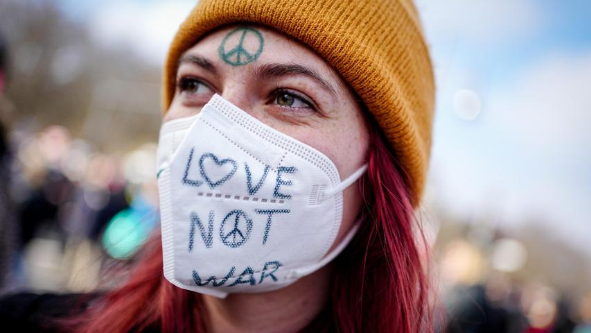 Eine Demonstrantin protestiert in der Nähe des Brandenburger Tores mit einer mit dem Satz "Love not war" beschrifteten Mundschutzmaske und einem Peace-Symbol auf der Stirn gegen den Krieg in der Ukraine.