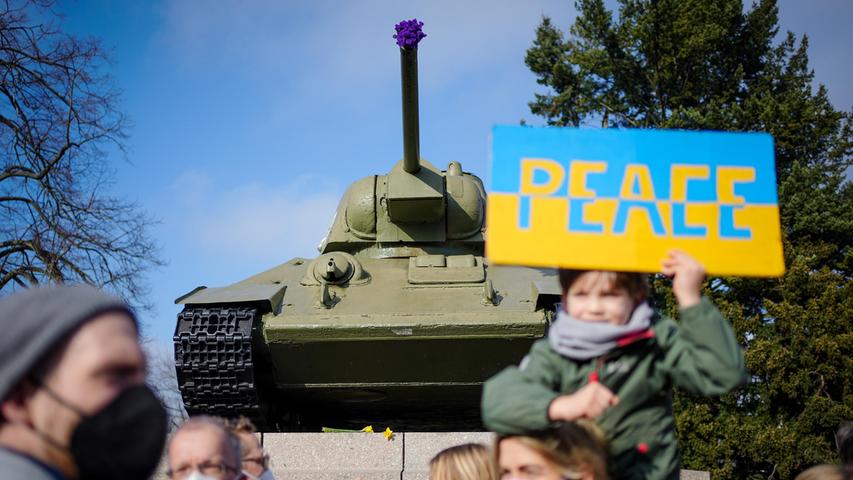 Teilnehmer demonstrieren mit einem Schild mit der Aufschrift "Peace" darauf an der Gedenkstätte für die getöteten sowjetischen Soldaten im Zweiten Weltkrieg vor einem sowjetischen Panzer vom Typ T34 gegen den Krieg in der Ukraine.