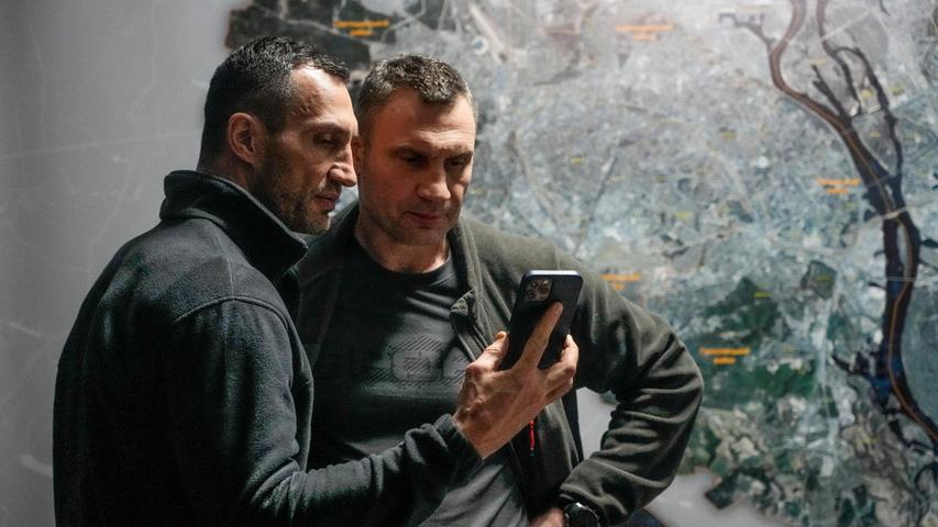 Vitali Klitschko (r), Bürgermeister von Kiew und ehemaliger Box-Profi, und sein Bruder Wladimir Klitschko, ebenfalls ehemaliger Box-Profi, schauen auf ein Smartphone im Rathaus in Kiew. Seit 2014 führt der Ex-Boxweltmeister Vitali die Stadt mit den 2,8 Millionen Einwohnern. "Die Nacht war schwer, doch es gibt keine russischen Truppen in der Stadt", sagt der 50-Jährige in einem Video, das er im sozialen Netzwerk Telegram veröffentlicht. Es gebe aber einzelne Saboteure, die ausfindig gemacht würden. Seit dem 24. Februar seien neun Zivilisten in Kiew getötet worden, darunter ein Kind, sagt er am Sonntag. Auch 18 ukrainische Sicherheitskräfte seien getötet worden. Verletzt wurden demnach bislang 106 Menschen, darunter 47 Zivilisten. Er erinnert an die Sperrstunden und mahnt, nur auf die Straße zu gehen, um in einem Bunker Schutz zu suchen.
