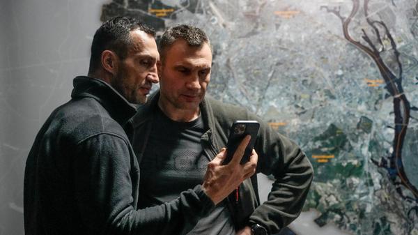 Vitali Klitschko (r), Bürgermeister von Kiew und ehemaliger Box-Profi, und sein Bruder Wladimir Klitschko, ebenfalls ehemaliger Box-Profi, schauen auf ein Smartphone im Rathaus in Kiew. Seit 2014 führt der Ex-Boxweltmeister Vitali die Stadt mit den 2,8 Millionen Einwohnern. "Die Nacht war schwer, doch es gibt keine russischen Truppen in der Stadt", sagt der 50-Jährige in einem Video, das er im sozialen Netzwerk Telegram veröffentlicht. Es gebe aber einzelne Saboteure, die ausfindig gemacht würden. Seit dem 24. Februar seien neun Zivilisten in Kiew getötet worden, darunter ein Kind, sagt er am Sonntag. Auch 18 ukrainische Sicherheitskräfte seien getötet worden. Verletzt wurden demnach bislang 106 Menschen, darunter 47 Zivilisten. Er erinnert an die Sperrstunden und mahnt, nur auf die Straße zu gehen, um in einem Bunker Schutz zu suchen.