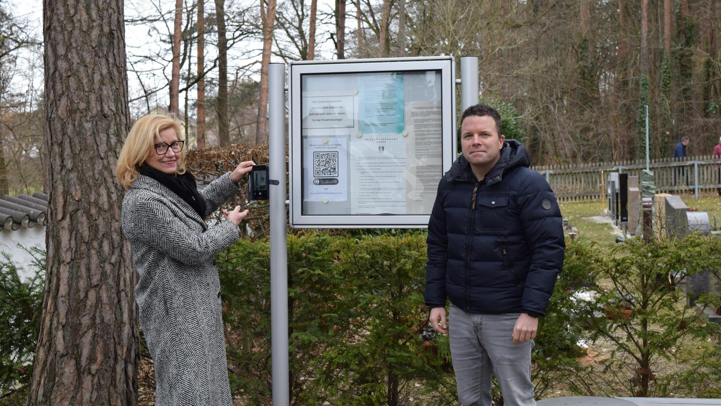 Eckentals Bürgermeisterin Ilse Dölle und Alexander Schmidt vom Ordnungsamt testen am Schaukasten des Eckenhaider Friedhofs den QR-Code für das digitale Verzeichnis der Gräber.