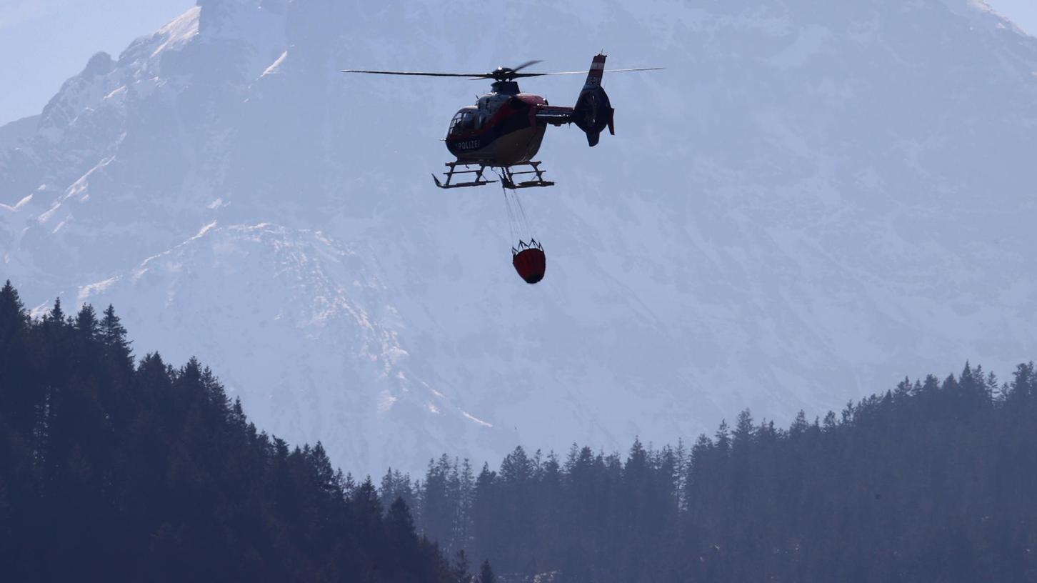 Ein Hubschrauber der österreichischen Polizei transportiert einen Behälter mit Wasser um damit letzte Brandherde in einem Bergwald zu löschen. Auch in Bayern ist derzeit die Waldbrandgefahr für März ungewöhnlich hoch.