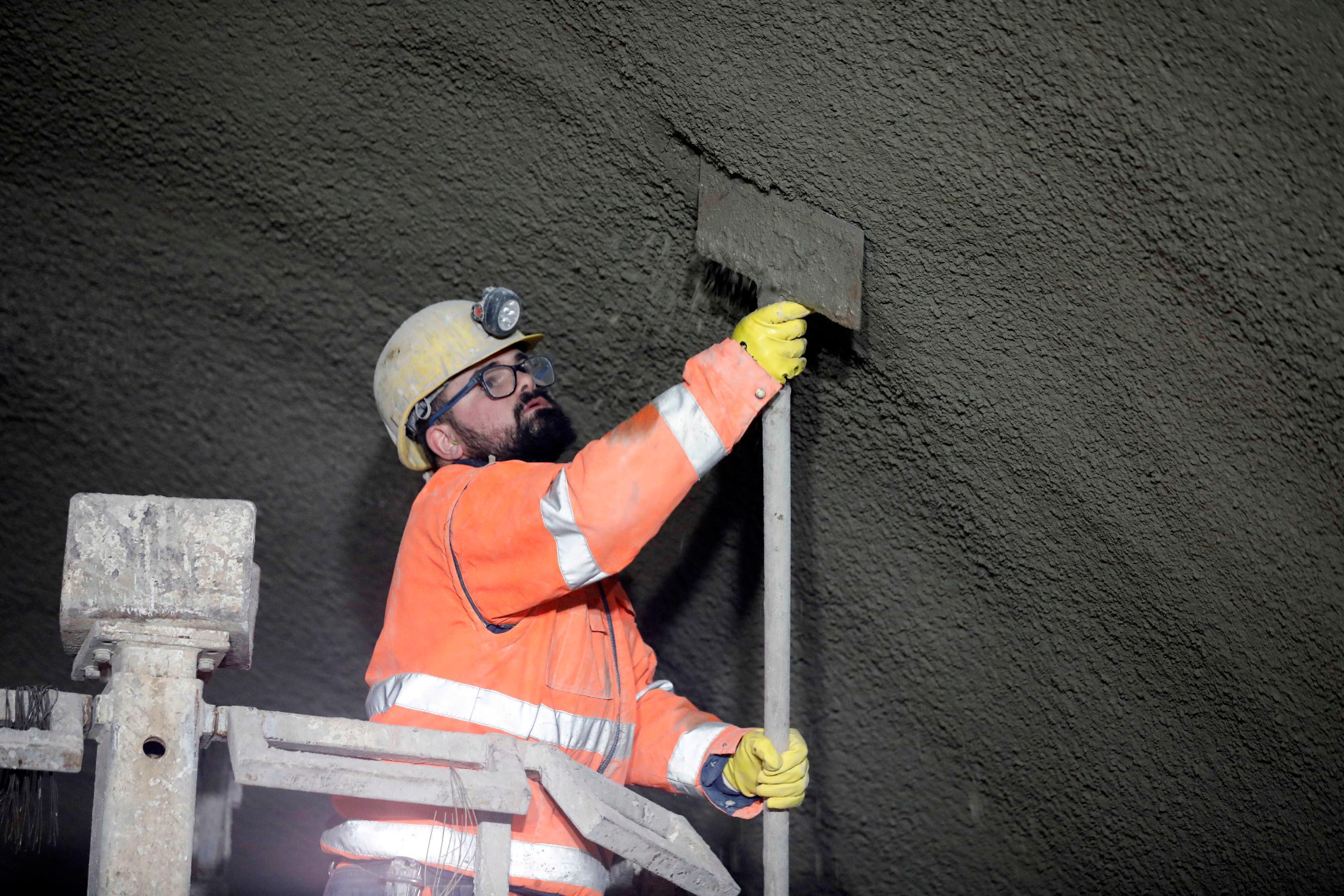 Von einer Hebebühne aus arbeitet ein Mineur mit einer Schaufel nach, wenn der Spritzbüffel zu viel Beton an einer Stelle verteilt hat.  