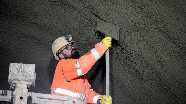 Von einer Hebebühne aus arbeitet ein Mineur mit einer Schaufel nach, wenn der Spritzbüffel zu viel Beton an einer Stelle verteilt hat.