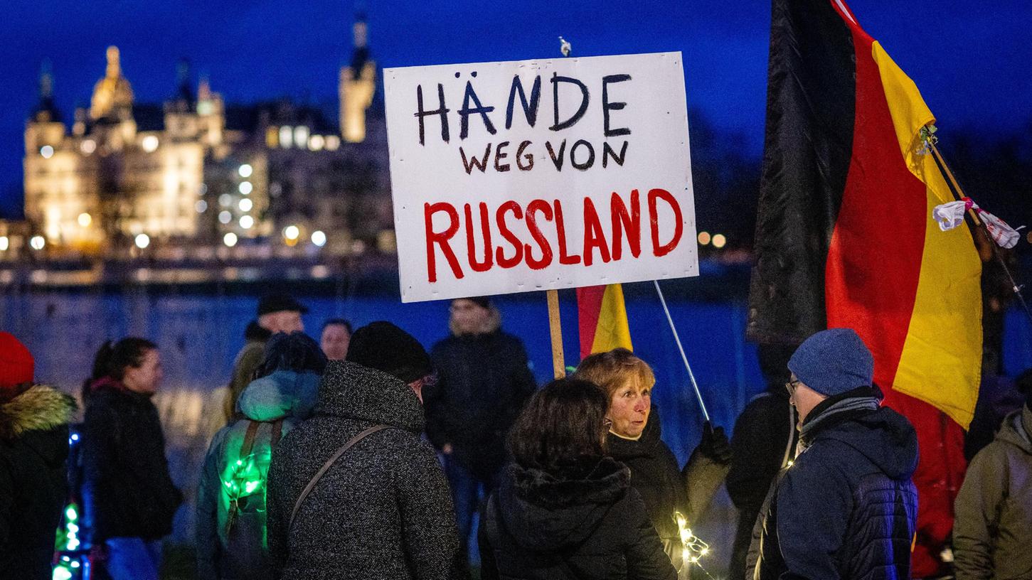 Teilnehmer der Protestaktion gegen die Corona-Schutzmaßnahmen halten am 21. Februar in Schwerin ein Schild mit der Aufschrift "Hände weg von Russland".