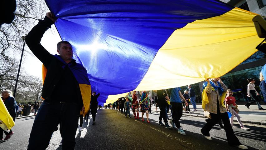 London: Menschen tragen eine große ukrainische Fahne während eines Solidaritätsmarsches für die Ukraine nach der russischen Invasion.