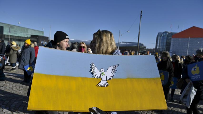 Finnland, Helsinki: Eine Demonstrierende hält eine ukrainische Fahne mit einer Friedenstaube während vor dem Parlamentsgebäude Menschen versammelt sind um für Frieden in der Ukraine zu demonstrieren.