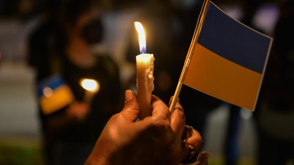 Malaysia, Kuala Lumpur: Eine Demonstrantin hält während einer Kerzenmahnwache vor der russischen Botschaft, um Russlands Invasion in die Ukraine zu verurteilen, eine Kerze und eine ukrainische Fahne in der Hand.