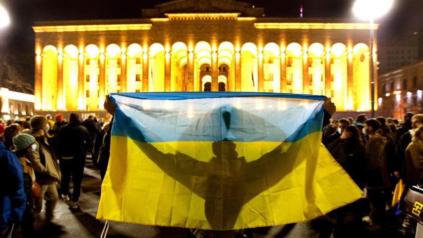Georgien, Tiflis: Ein Demonstrant hält eine ukrainische Fahne vor dem georgischen Parlament während einer Demonstration gegen Russlands Angriff auf die Ukraine hoch. Trotz der internationalen Appelle für ein Ende des Kriegs hat Russland seine Angriffe auf die Ukraine verschärft. 
