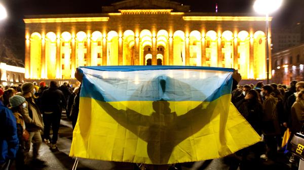 Georgien, Tiflis: Ein Demonstrant hält eine ukrainische Fahne vor dem georgischen Parlament während einer Demonstration gegen Russlands Angriff auf die Ukraine hoch. Trotz der internationalen Appelle für ein Ende des Kriegs hat Russland seine Angriffe auf die Ukraine verschärft.