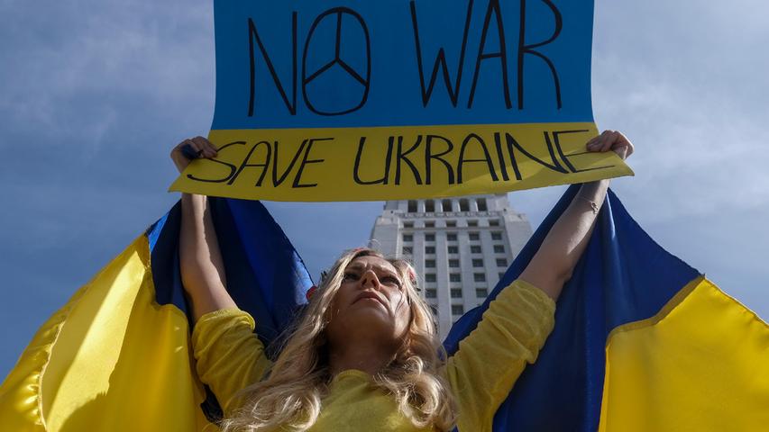 USA, Los Angeles: Eine Demonstrantin ist bei einem Protest gegen Russlands Invasion in die Ukraine in den Farben der ukrainischen Flagge gekleidet und hält ein Schild mit ihren Forderungen.