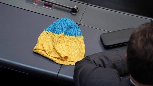 Deutscher Bundestag 20. Plenarsitzung: Ein Abgeordneter hat eine Muetze und Kappe in den Farben der Flagge der Ukraine neben sich liegen.