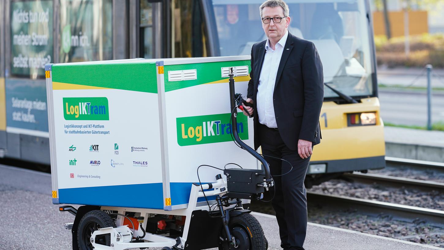 Michael Frey, stellvertretender Leiter des Instituts für Fahrzeugsystemtechnik am Karlsruher Institut für Technologie (KIT), steht mit dem Prototyp eines Ladungsträgers an einer Straßenbahnhaltestelle. Das kleine Fahrzeug soll zum automatisierten Pakettransport in der Straßenbahn genutzt werden.