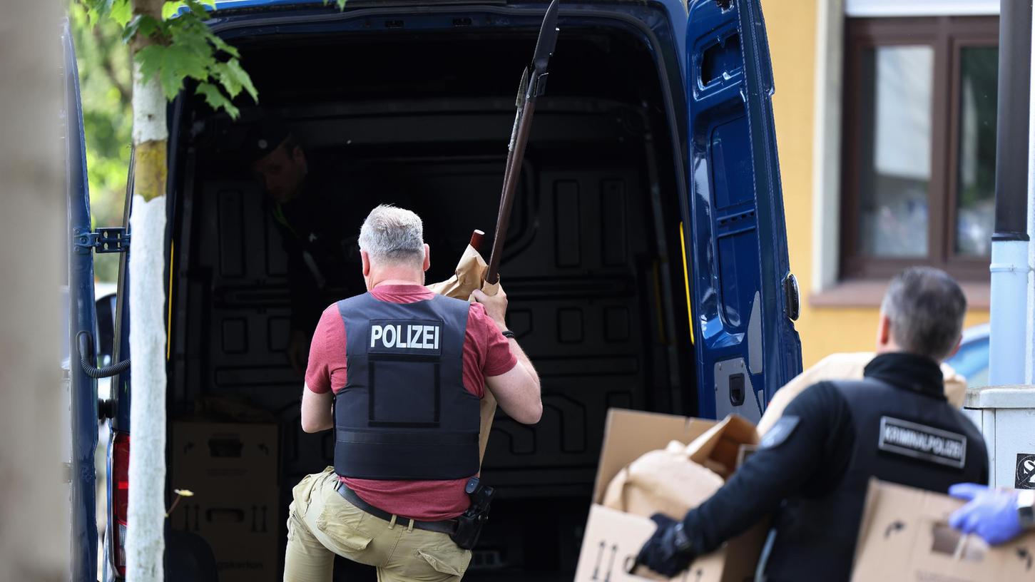 Polizisten tragen Gegenstände, darunter mehrere Stichwaffen und Speere, aus dem Wohnhaus des Verdächtigen. 