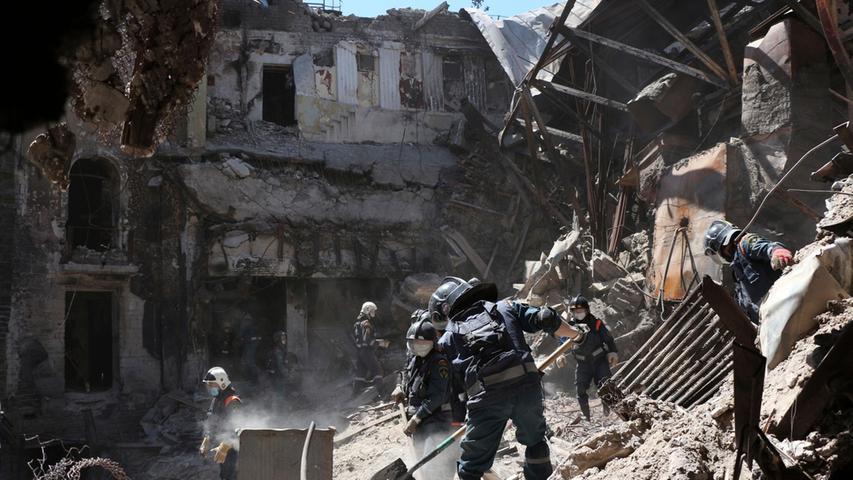 Mitarbeiter des Ministeriums für Notsituationen der selbst ernannten Volksrepublik Donezk räumen Trümmer des schwer beschädigten Theatergebäudes in Mariupol zur Seite.