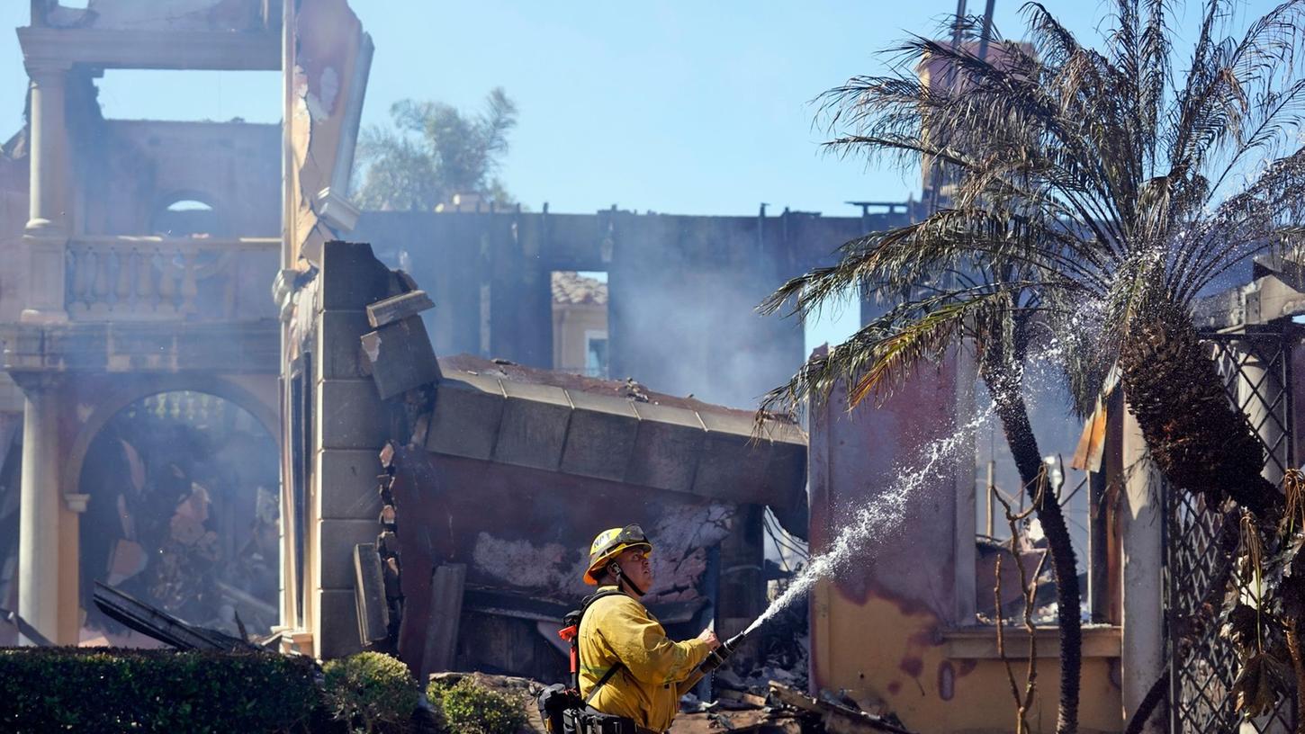Der Feuerwehrmann Mike Mejia vom National City Fire Dept. löscht noch brennende Stellen an einem Haus nach dem Küstenfeuer in Laguna Niguel.