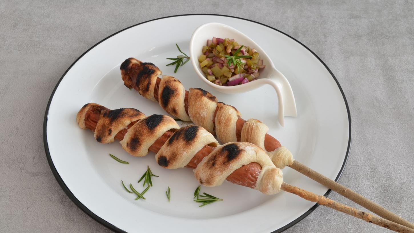 Das Stockbrot wird schlangenmäßig um den Hotdog gewickelt und gegrillt. Das Stockbrot wird schlangenmäßig um den Hotdog gewickelt und gegrillt.