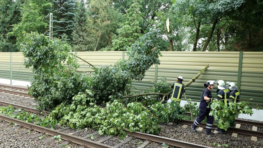 Feuerwehrleute beseitigen nach einem Unwetter umgestürzte Bäume auf einer Bahnstrecke.