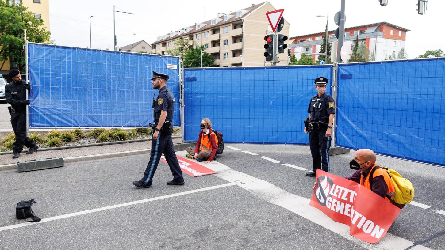 Polizisten stellen einen Sichtschutz rund um Aktivisten der Gruppierung "Letzte Generation" auf. Die Aktivisten haben sich zuvor mit den Händen auf eine Ausfahrt vom Mittleren Ring geklebt. 