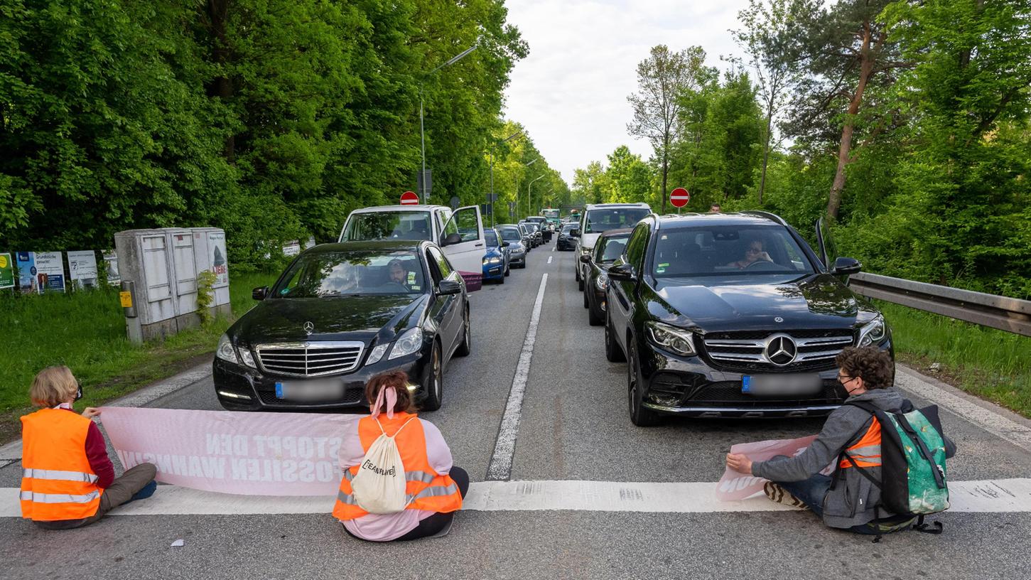 Klima-Aktivisten der Gruppe "Letzte Generation" blockieren mit Plakaten in der Hand das Ende einer Autobahnabfahrt an einer Kreuzung.
