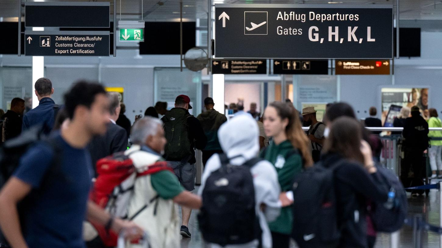 Passagiere stehen mit ihrem Gepäck vor der Sicherheitskontrolle am Flughafen.
