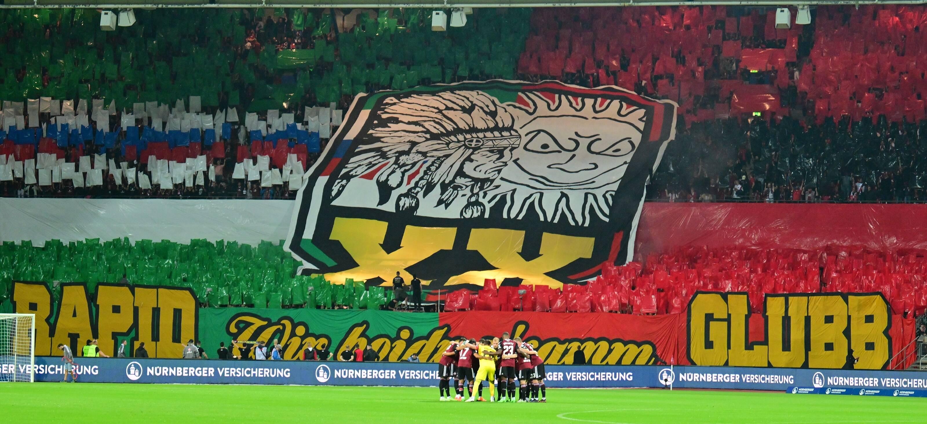 <p>Anschließend wurde eine Blockfahne präsentiert, die das Indianer-Wappen der Ultras Rapid und das Sonnenlogo der Ultras Nürnberg zeigt. Darunter eine römische 20 - für das 20-Jährige bestehen der Freundschaft.</p>
