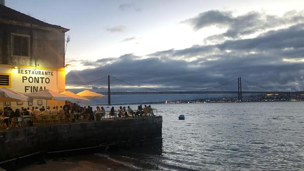 Entlang der Küstenpromenade gibt es mehrere Restaurants und Cafés. Wer direkt am Wasser sitzen und den Blick auf die portugiesische Golden-Gate-Bridge genießen will, sollte lieber vorher einen Platz reservieren. Der Blick auf Lissabon zieht die Menschen hier magisch an. Die Gegend wirkt zwar stellenweise heruntergekommen, erfindet sich aber gerade neu. Ein besonderer Charme. Die spannende Reisereportage zu dieser Bildergalerie lesen Sie unter www.nn.de/leben/reisen