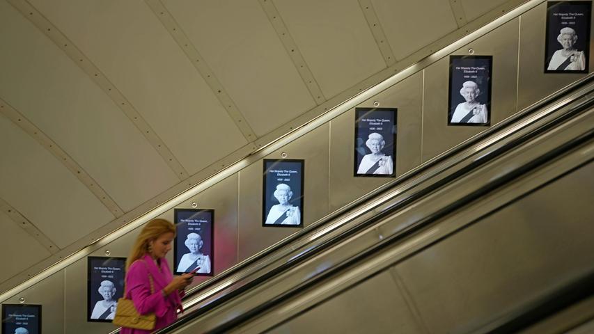 09.09.2022, Großbritannien, London: Eine Frau geht an Bildern von Königin Elizabeth II. vorbei, die an einer Rolltreppe in einer U-Bahn-Station ausgestellt sind. Die britische Königin Elizabeth II. ist am 08.09.2022 im Alter von 96 Jahren gestorben.