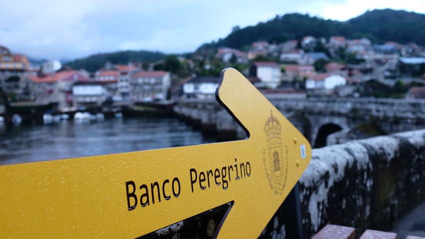 Einen gelben Pfeil, den man nicht übersehen kann. Wer kurz ausruhen möchte, kann dies auf einer "Banco Peregrino" tun, wie hier an der Ponte Medieval de Pontesampaio in Galizien. 
