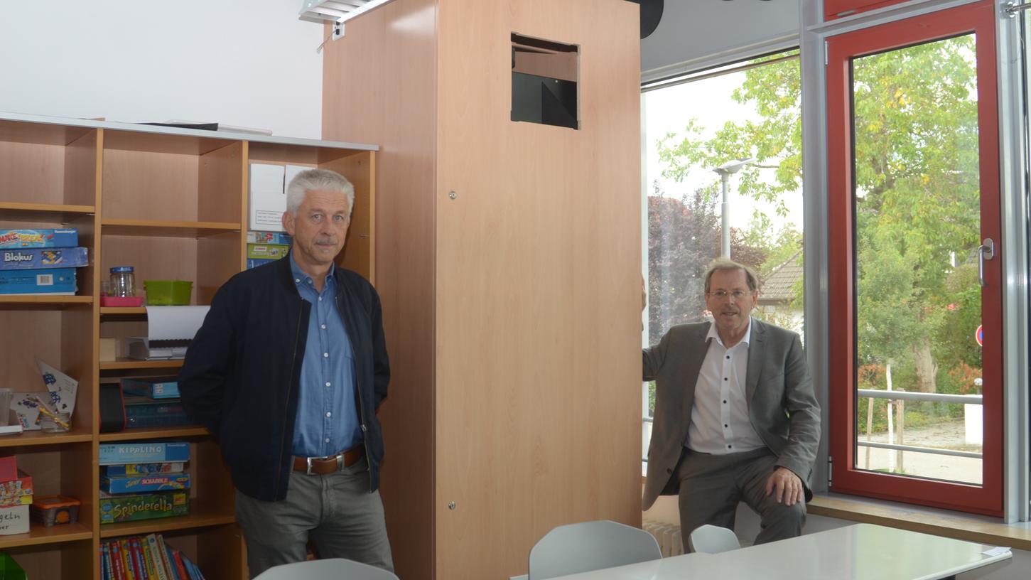 Die Lebenshilfe-Verantwortlichen Werner Mönikheim (links) und Hans Herold zeigen den "Schrank", in dem eine Raumluft-Tauscher-Anlage installiert ist. 

