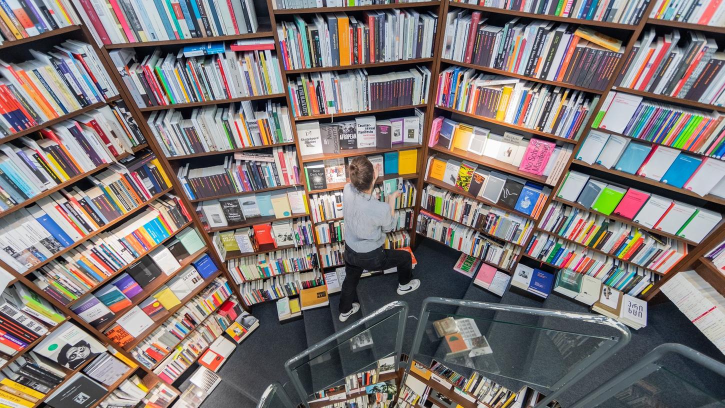 Eine Frau sortiert Bücher in die Regale einer Buchhandlung ein. Eine Frau sortiert Bücher in die Regale einer Buchhandlung ein.