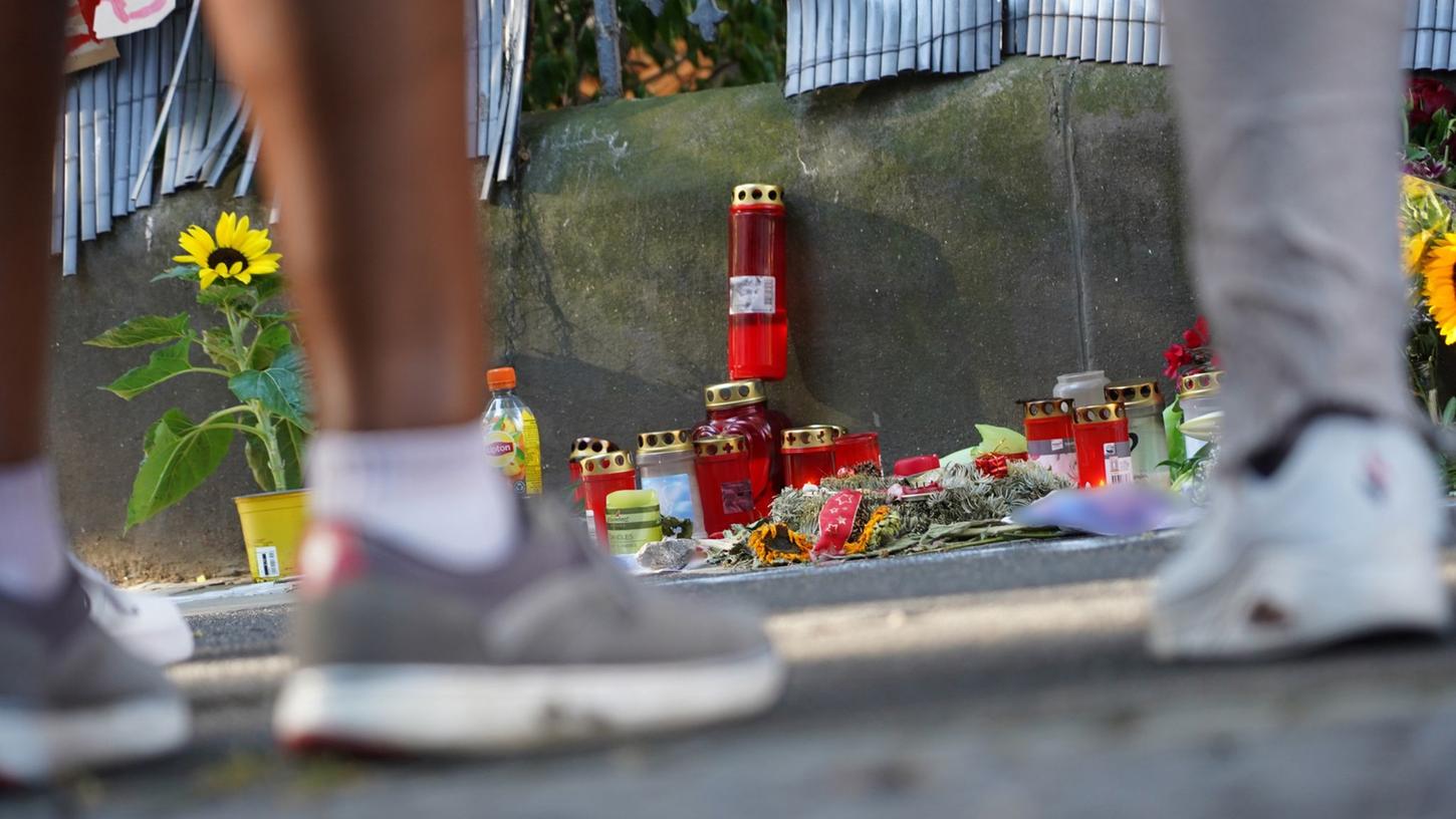 Menschen stehen vor einem Zaun, an dem mit Kerzen und Blumen eines von der Polizei erschossenen Jugendlichen gedacht wird.