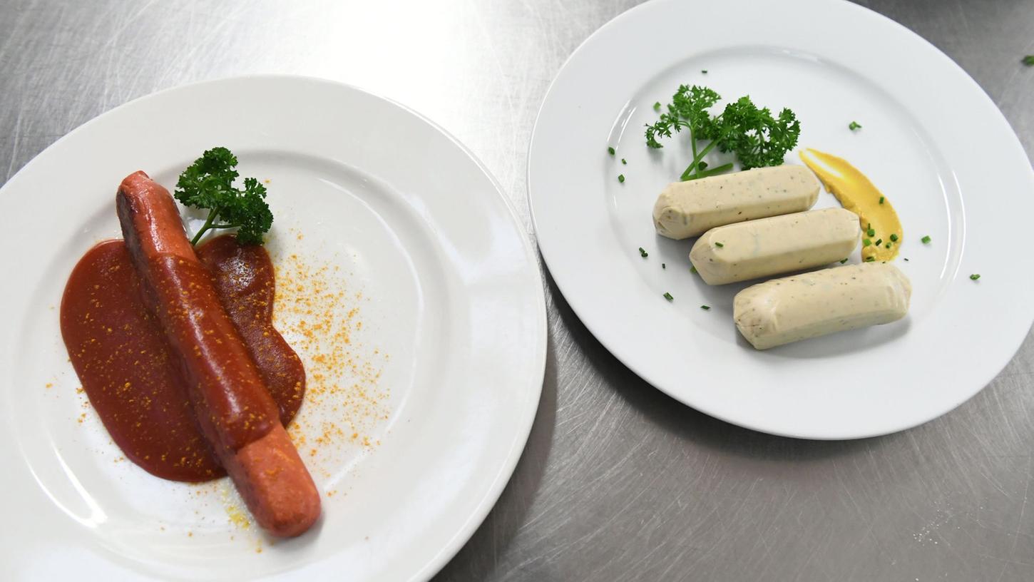 Eine vegane Currywurst und vegane Weißwürste liegen auf Tellern an der Essensausgabe im Hofbräuzelt auf dem Oktoberfest. Eine vegane Currywurst und vegane Weißwürste liegen auf Tellern an der Essensausgabe im Hofbräuzelt auf dem Oktoberfest.