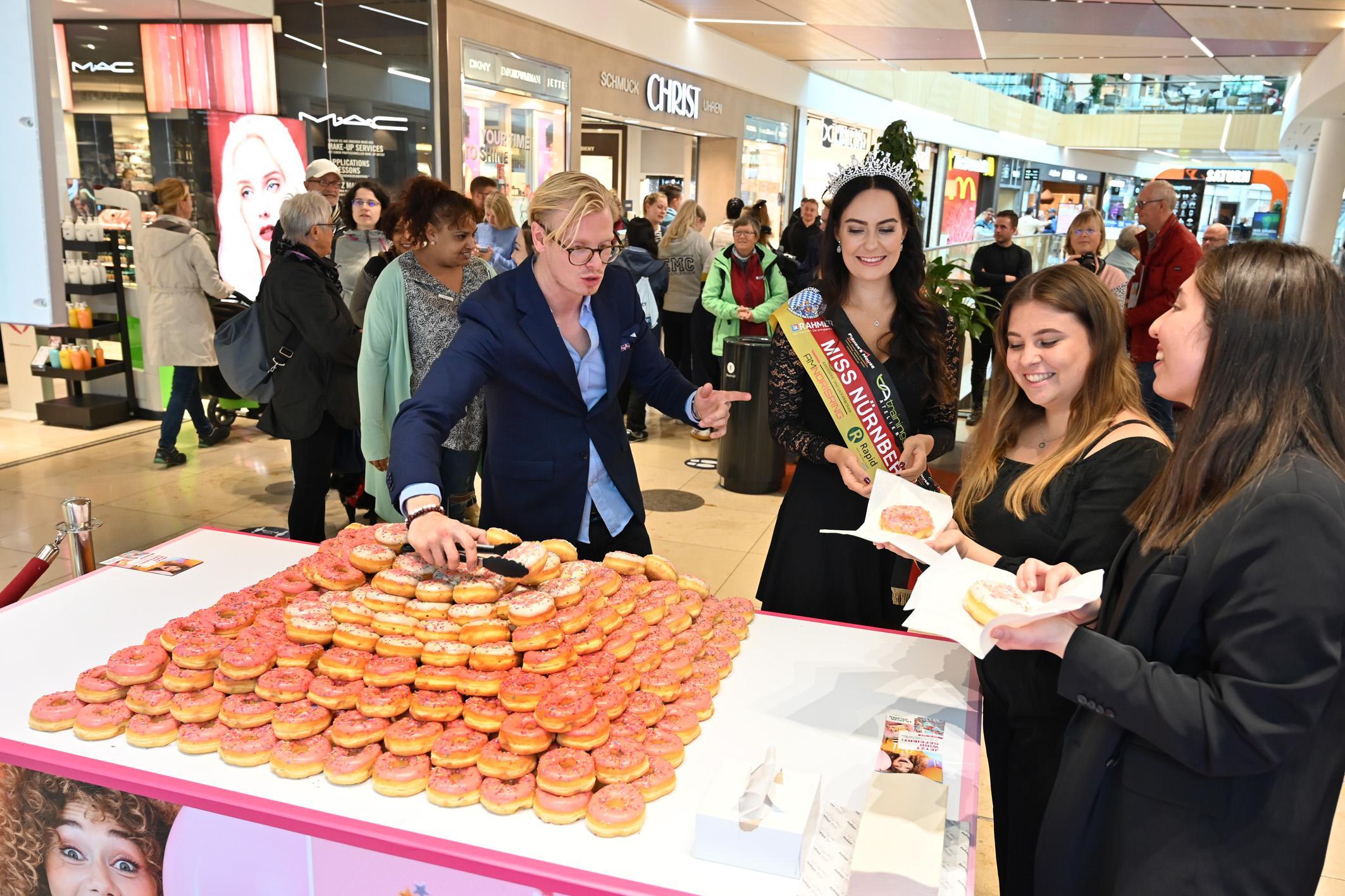 Die Erlangen Arcaden feiern "15 Jahre im Herzen der Stadt". Miss Bayern Carina Schätz und Moderator Constantin Greif verteilen Donats.