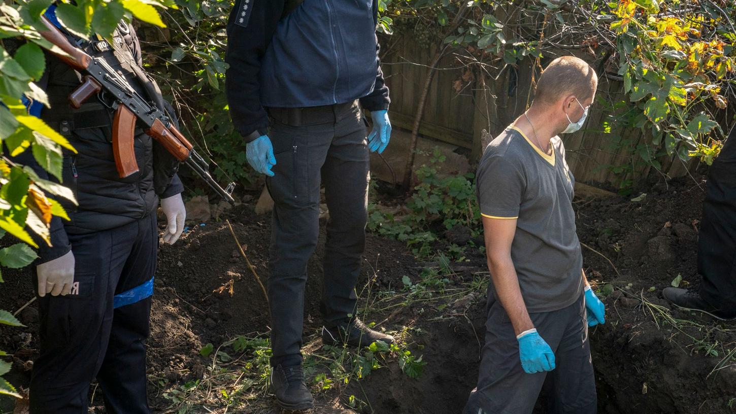 Beamte exhumieren die erste von zwei Leichen aus einem Grab als Teil einer Untersuchung von Kriegsverbrechen in dem ukrainischen Dorf Hrakowe.