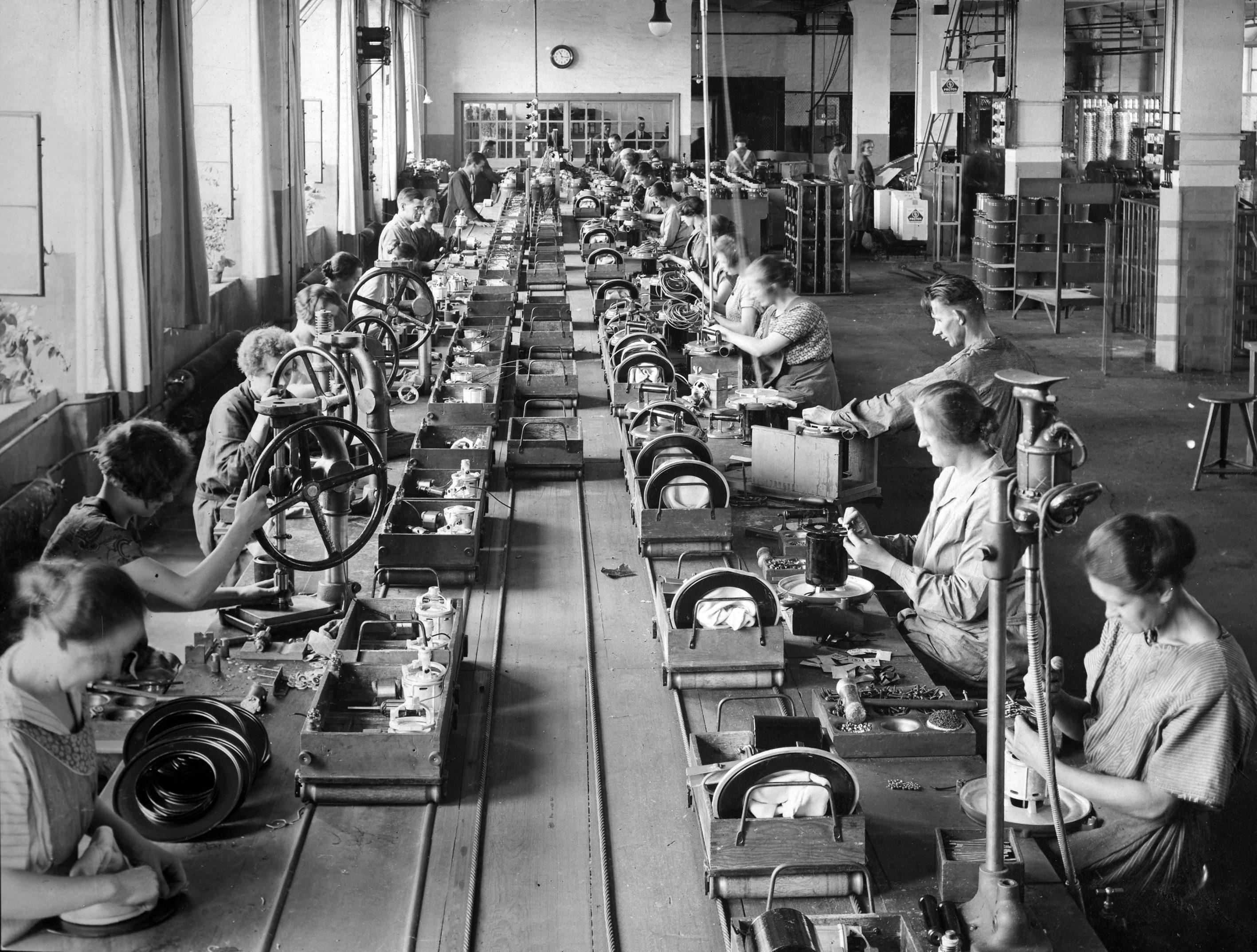 Zu Beginn der 1920er Jahre treibt das Unternehmen die Standardisierung und Reorganisation der Haus- und Rundfunkgerätefertigung in Richtung Fließbandfertigung voran. Weitere Produkte folgen bald: Hier sieht man Frauen und Männer im Dezember 1924 im Berliner Elektromotorenwerk (Elmowerk) bei der Montage von Staubsaugern.