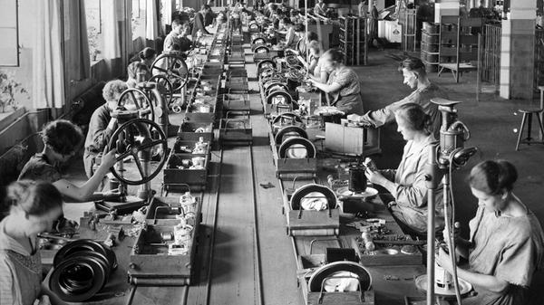 Zu Beginn der 1920er Jahre treibt das Unternehmen die Standardisierung und Reorganisation der Haus- und Rundfunkgerätefertigung in Richtung Fließbandfertigung voran. Weitere Produkte folgen bald: Hier sieht man Frauen und Männer im Dezember 1924 im Berliner Elektromotorenwerk (Elmowerk) bei der Montage von Staubsaugern.