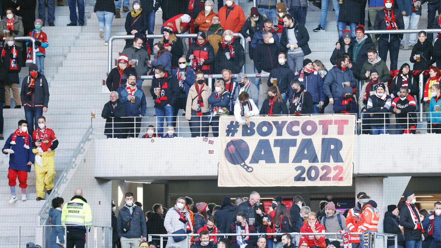 Fans des SC Freiburg stehen auf der Tribüne vor und hinter einem Banner mit der Aufschrift ·#BOYCOTT QATAR 2022·