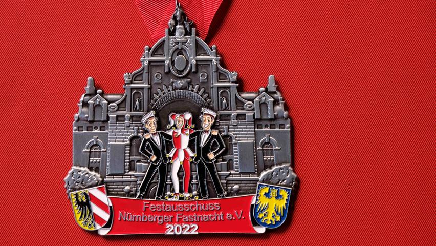 Der Faschingsorden zeigt zwei Karnevalisten und Till Eulenspiegel in der Mitte. Alle drei stehen vor dem Opernhaus Nürnberg.