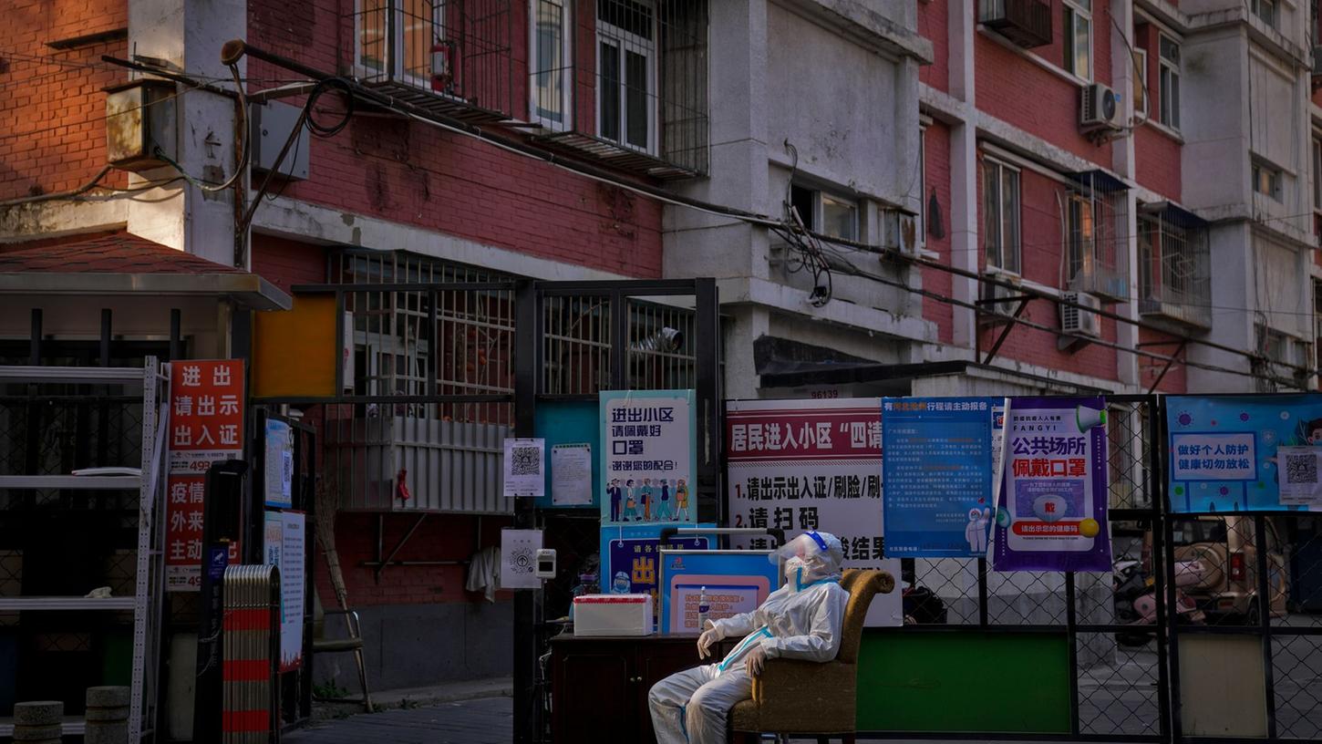 Ein Wachmann im Schutzanzug sitzt an einem Eingangstor zu einem Wohnviertel in Peking.