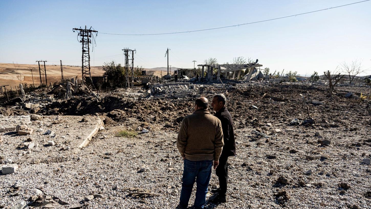 Zwei Männer begutachten Schäden in einem Gebiet um ein Elektrizitätswerk in Nordsyrien nach türkischen Luftangriffen.