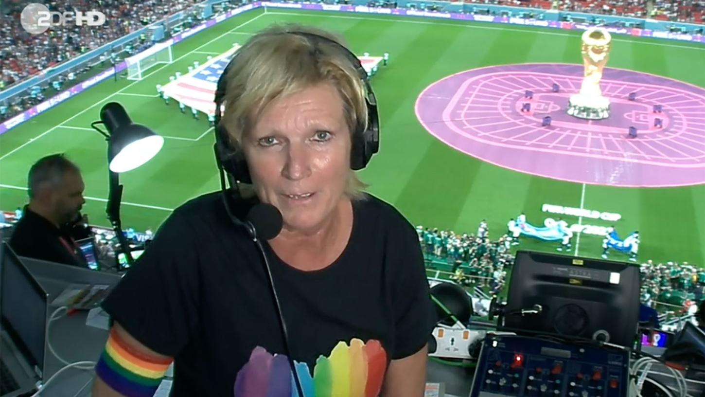 ZDF-Kommentatorin Claudia Neumann mit Regenbogen-Armbinde und einem schwarzen T-Shirt, auf dem ein Herz in den Regenbogenfarben abgebildet ist.