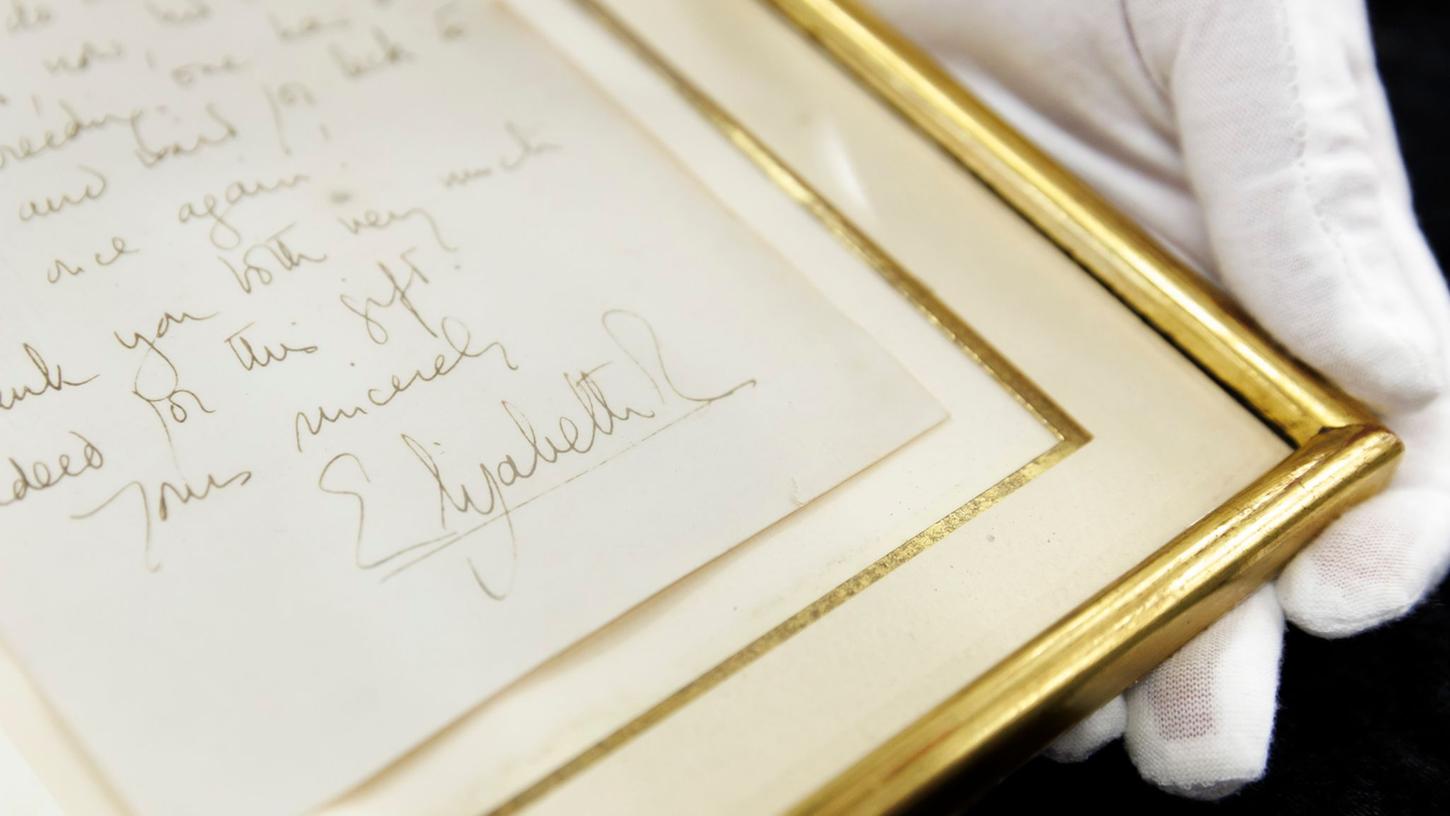 Ein handgeschriebener Brief von Königin Elizabeth II. (1926-2022) aus dem Jahr 1966 wird versteigert. Die Unterschrift der Queen ist auf einer Kopie der Rückseite zu sehen, welche dem eingerahmten Brief beiliegt.