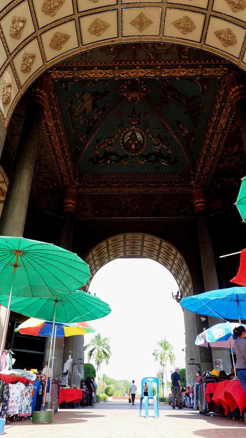 Souvenirstände mit Schirmen warten unterm Bogen auf Touristen.
