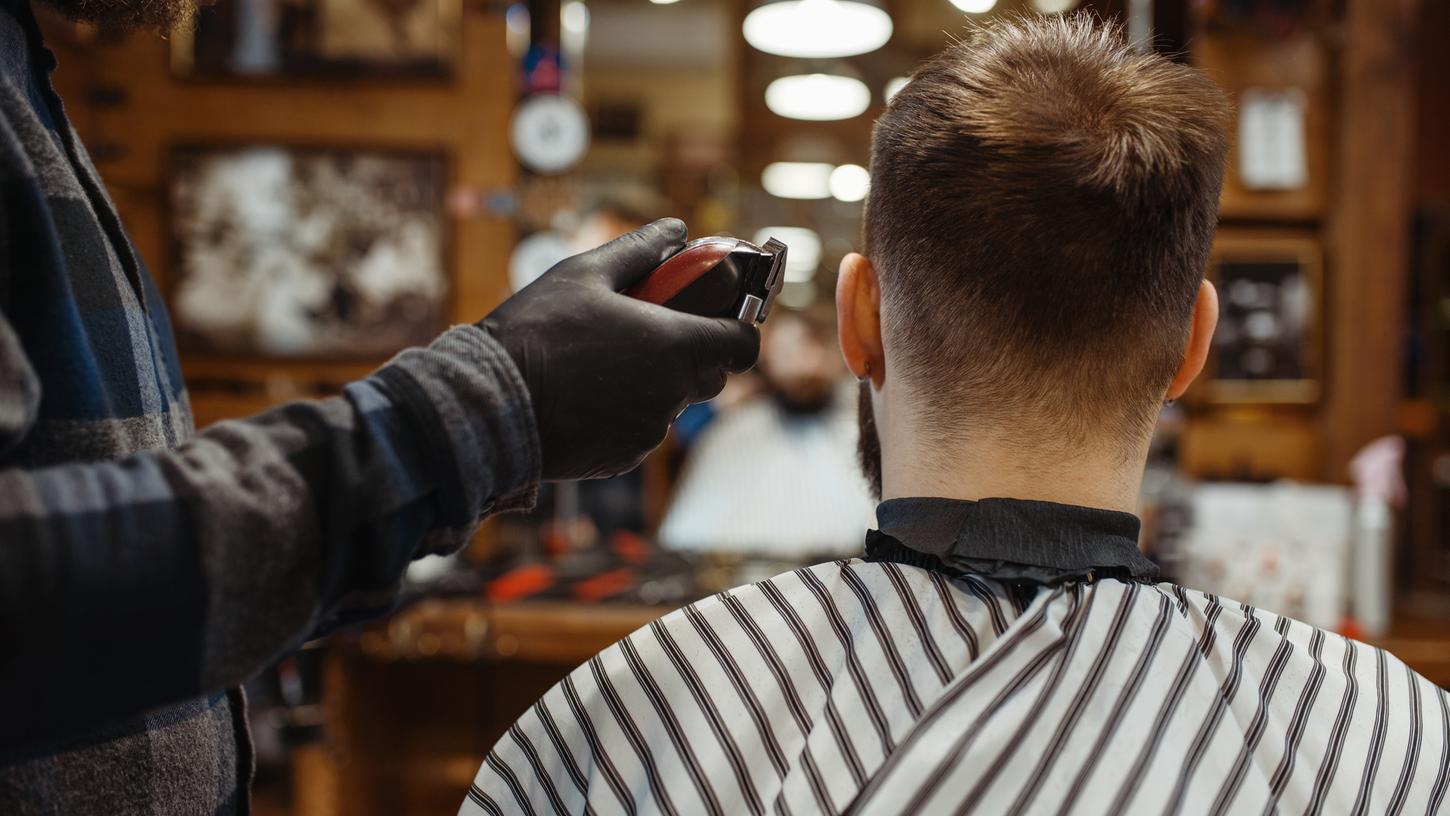 Ein Angestellter in einem Barbershop schneidet die Haare eines Kunden (Symbolbild).   