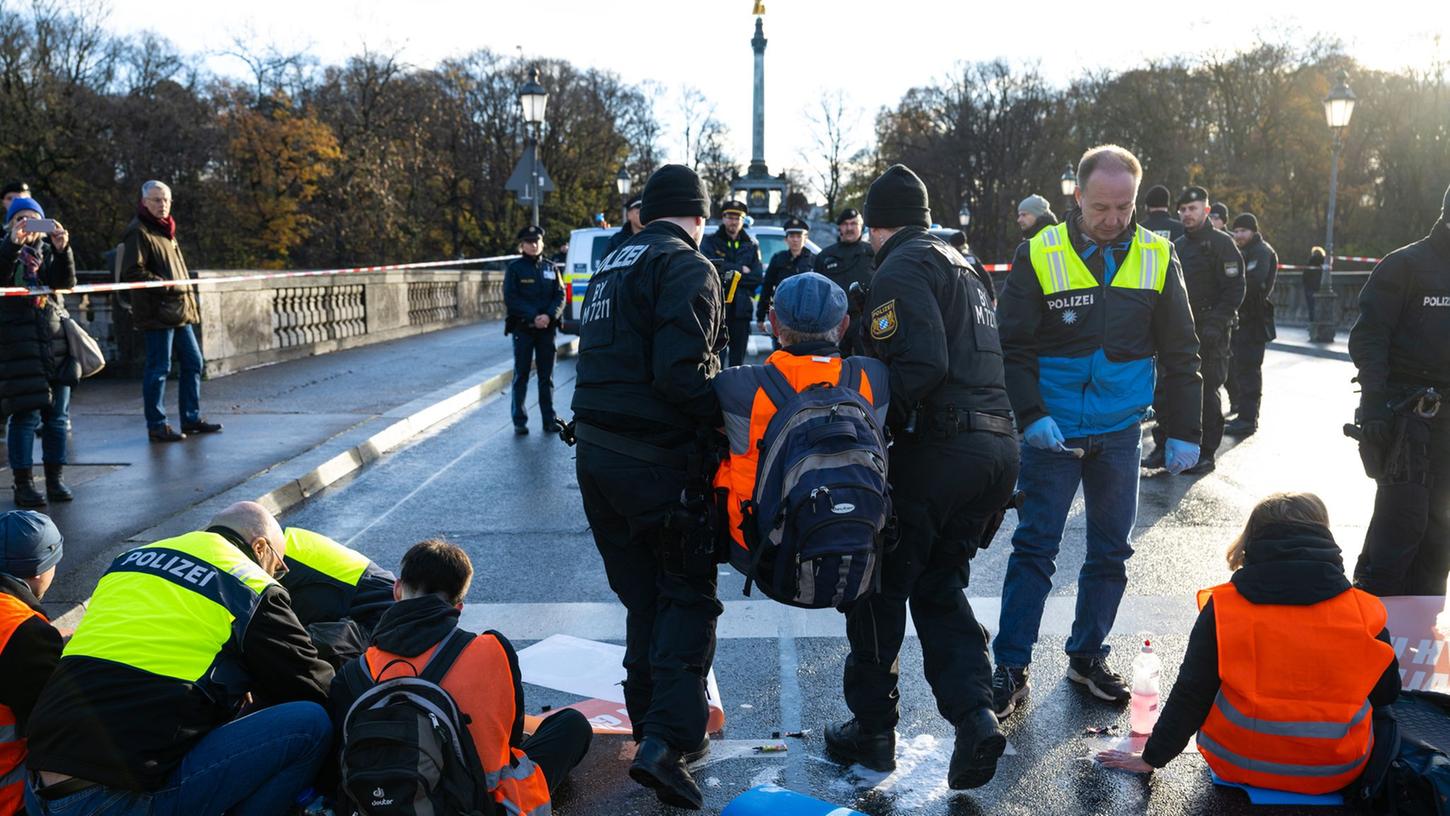 Polizisten tragen in München einen Klimaaktivisten der "Letzten Generation" weg, der sich zuvor auf der Prinzregentenstraße auf den Asphalt geklebt hatte. Polizisten tragen in München einen Klimaaktivisten der "Letzten Generation" weg, der sich zuvor auf der Prinzregentenstraße auf den Asphalt geklebt hatte.