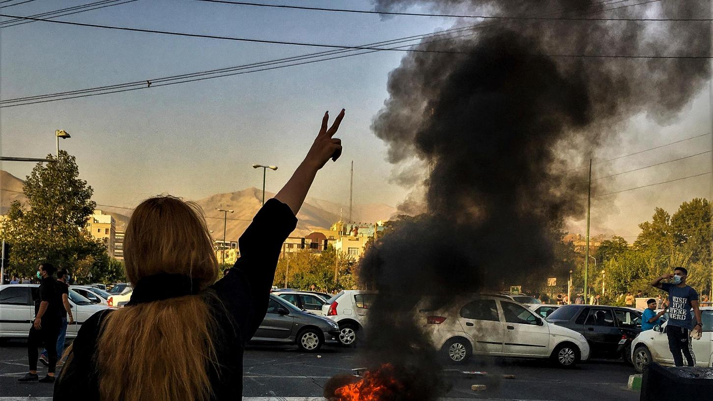 Eine Frau steht in Teheran während einer Demonstration nach dem Tod der 22-jährigen Mahsa Amini vor einem brennenden Autoreifen und zeigt das Victory-Zeichen.
