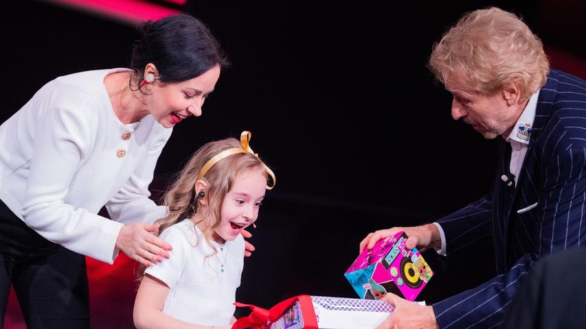 Amelia (M) erhält beim RTL-Jahresrückblick "Menschen, Bilder, Emotionen 2022" ein Geschenk von Moderator Thomas Gottschalk, daneben steht ihre Mutter.