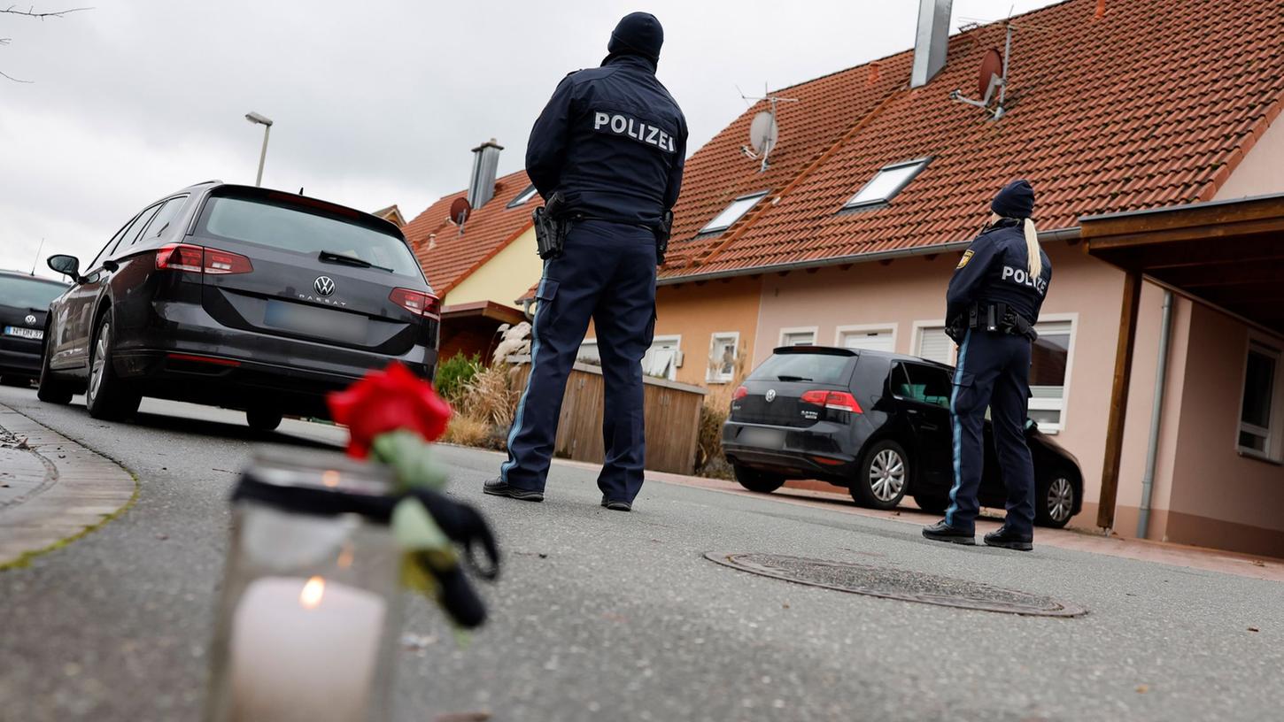 Polizisten stehen neben einer Trauerkerze vor einem Haus. Eine Gewalttat hat den 6800-Einwohner-Ort Weisendorf nahe Erlangen in Mittelfranken erschüttert.